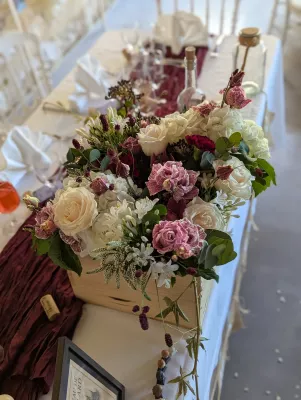Centre de table de mariage bohème avec roses crème, hortensias blancs, œillets bordeaux et feuillage dans une boîte en bois.