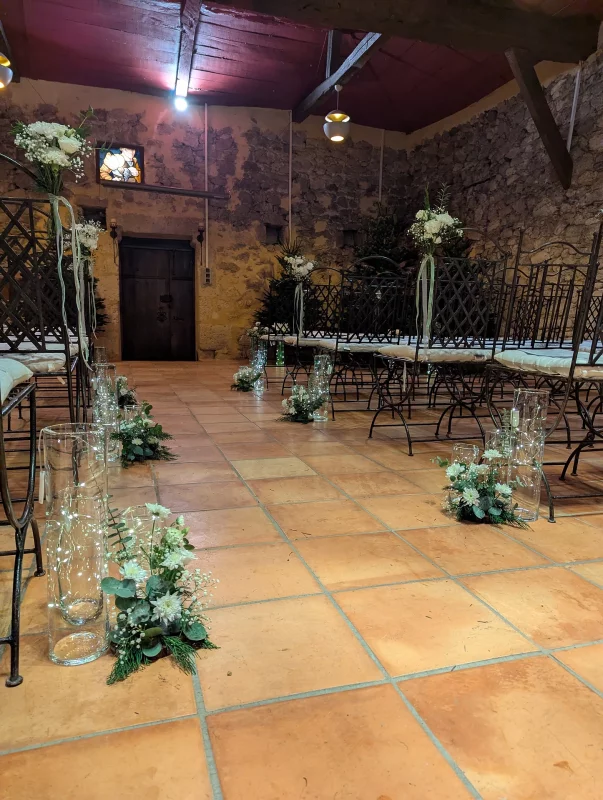 Allée de cérémonie décorée de guirlandes de sapin, chrysanthèmes blancs, eucalyptus et vases lumineux, mariage classique.