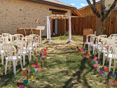 Aménagement de cérémonie extérieure champêtre avec arche fleurie, chaises décorées et allée colorée.