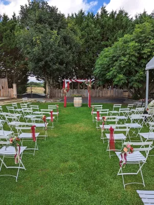 Vue d'ensemble d'une cérémonie de mariage extérieure champêtre avec une arche florale bordeaux et pêche, et des chaises blanches décorées, à Génissac.