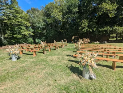 Decoration de ceremonie de mariage exterieure style boheme avec des bancs en bois, compositions florales roses et pampas.