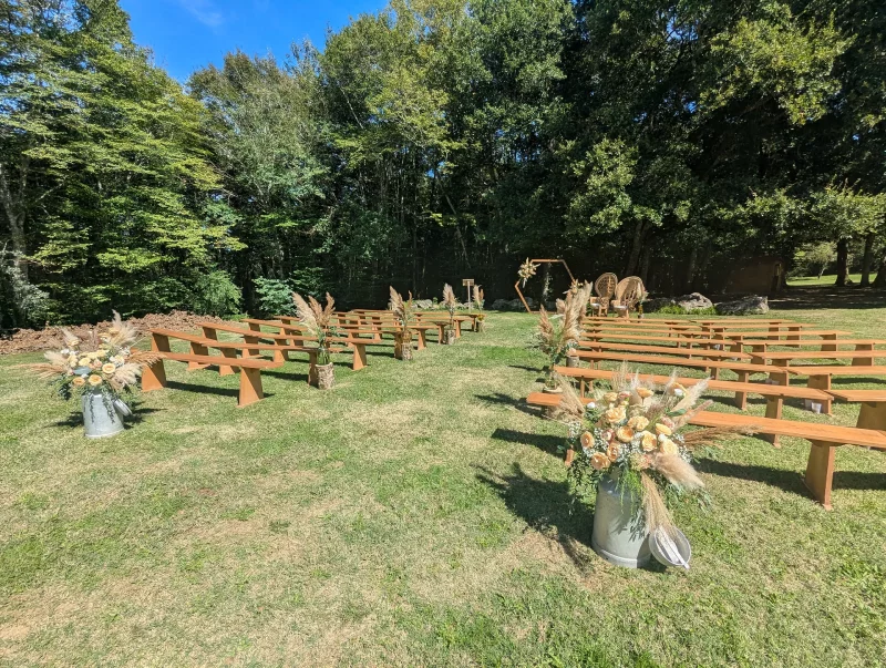 Outdoor wedding ceremony décor, bohemian style, with wooden benches, pink roses and pampas grass floral arrangements.