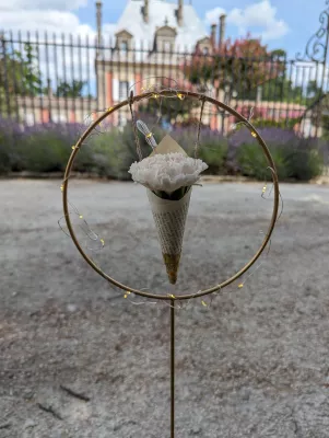 Décoration suspendue minimaliste pour cérémonie, avec un œillet blanc dans un cône en papier sur un cercle doré lumineux.
