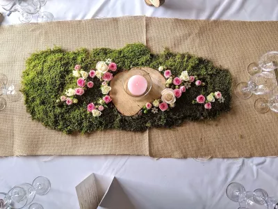 Chemin de table champêtre avec mousse végétale, roses roses et crème, et rondin de bois pour un mariage naturel.