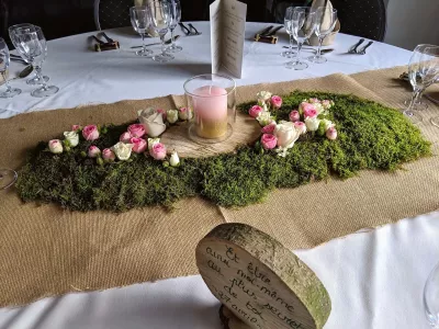 Chemin de table champêtre pour mariage, avec mousse, roses roses et crème, rondin de bois et bougie.