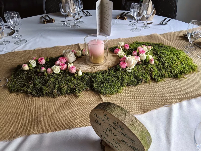 Rustic-chic wedding tablescape, featuring moss, pink and cream roses, a wooden slice, and a candle.