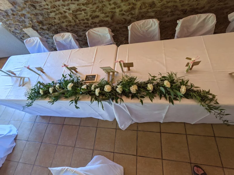 Chemin de table floral champêtre avec roses blanches et abondant feuillage d'eucalyptus pour la table d'honneur d'un mariage.