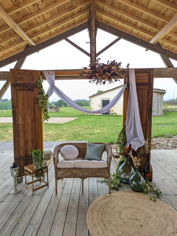 Rustic-chic photo corner with rattan sofa, orange and terracotta dried flowers, and white drapery.
