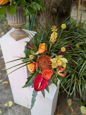 Colonne décorative exotique avec anthurium rouge, roses orange, orchidées et feuillage tropical pour un mariage.