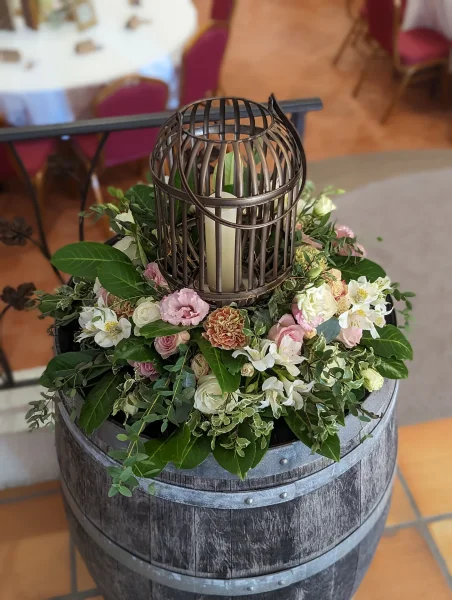 Colonne décorative champêtre avec un arrangement floral de roses, œillets, eucalyptus et une lanterne en métal.