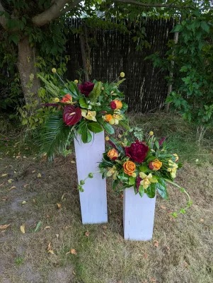 Deux colonnes décoratives exotiques avec anthurium, roses orange, orchidées cymbidium et feuillage tropical pour un mariage.