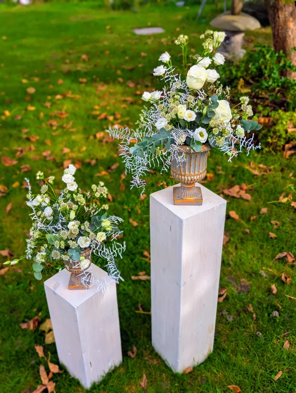 Two classic floral arrangements on columns, with white roses and lisianthus, eucalyptus and frosted foliage for an autumn wedding.