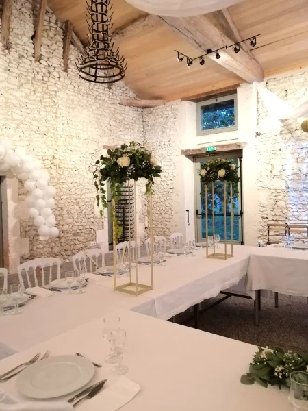 Gros plan sur les majestueuses colonnes florales dorées, ornées de roses blanches et d'eucalyptus luxuriant, encadrant l'espace repas pour un mariage champêtre moderne.
