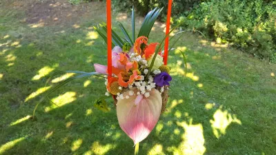 Composition florale suspendue pour un mariage, avec ananas, anthurium rose, gloriosa orange et feuillage tropical.