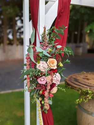 Composition florale asymétrique pour arche de mariage, avec amarante tombante, roses pêches et feuillage d'eucalyptus, style bohème.