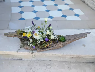 Boho botanical floral arrangement on driftwood with white roses, purple campanulas, and succulents.
