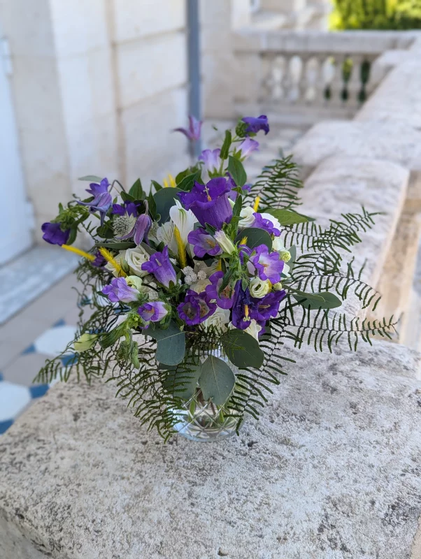 Lush bohemian floral arrangement featuring purple campanulas, white roses and ferns for a wedding.