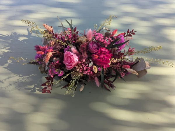 Composition florale horizontale champêtre sophistiquée avec dahlias fuchsia, roses et feuillages pour mariage.