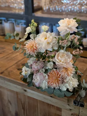 Composition florale de mariage classique avec pivoines, dahlias pêche, roses et eucalyptus sur un bar en bois.