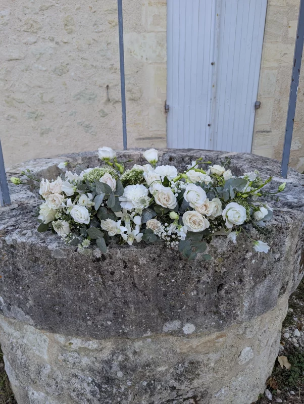 Sophisticated country-style floral arrangement with cream roses and eucalyptus on a stone well for a wedding.
