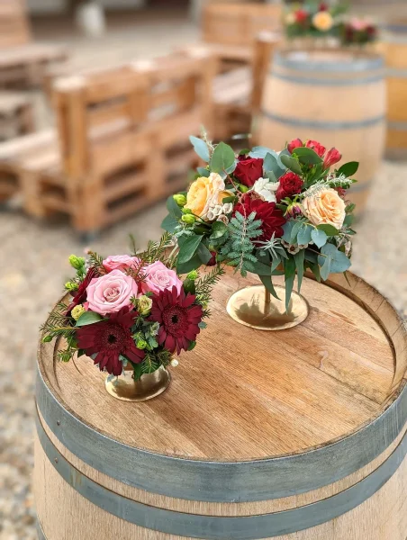Compositions florales champêtres avec gerbera bordeaux, roses roses et pêche sur tonneaux, mariage d'été.