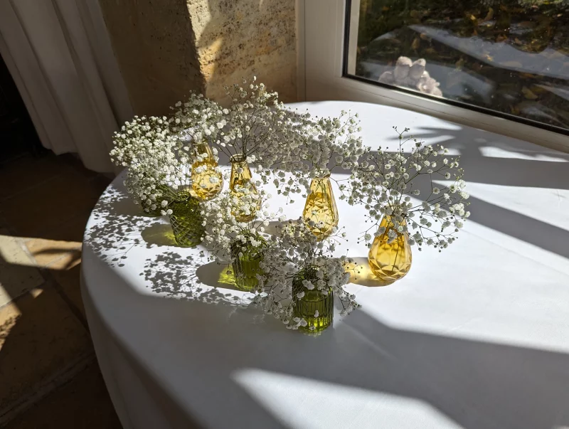 Composition de table champêtre avec gypsophile dans des mini-vases en verre vert et jaune.
