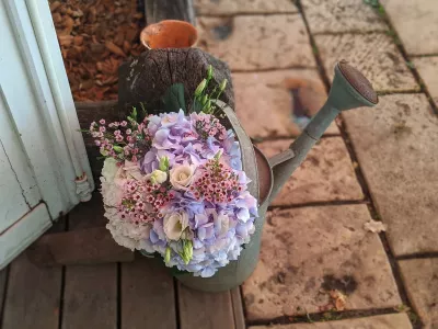 Composition florale bohème dans un arrosoir vintage, avec hortensias roses et bleus, roses blanches et waxflower.