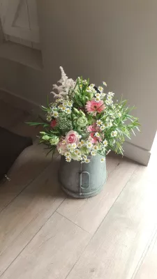 Composition florale de mariage champêtre avec marguerites, roses, astilbe et gérberas roses dans un seau galvanisé.