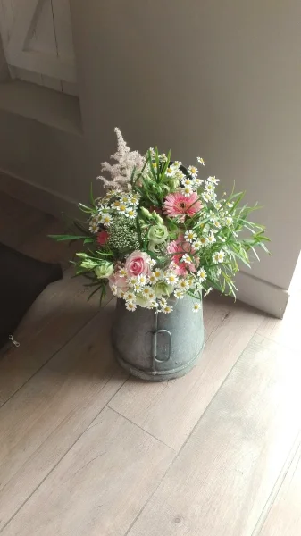 Composition florale de mariage champêtre avec marguerites, roses, astilbe et gérberas roses dans un seau galvanisé.
