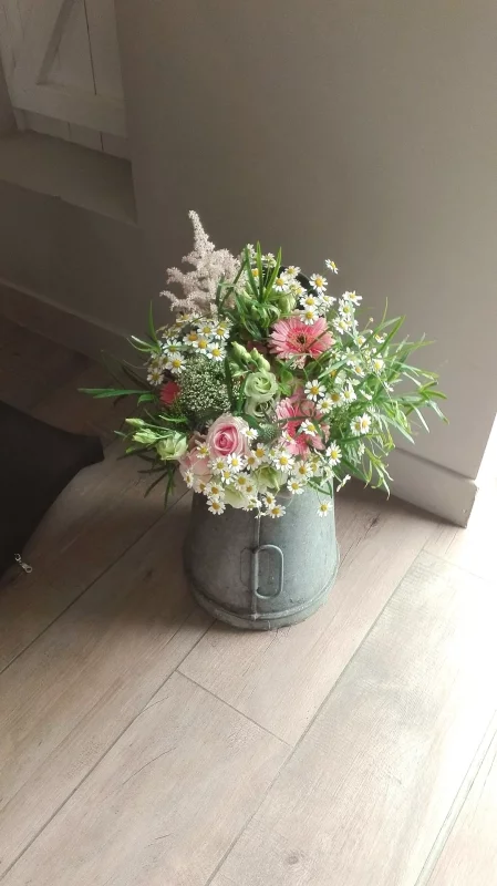 Composition florale de mariage champêtre avec marguerites, roses, astilbe et gérberas roses dans un seau galvanisé.