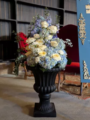 Décoration florale de mariage classique avec roses crème, hortensias bleus et feuillage d'eucalyptus dans une urne noire.