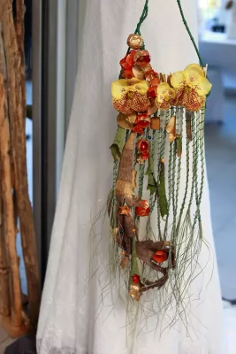 Composition bohème suspendue avec orchidées jaunes, éléments séchés, baies rouges et branches.