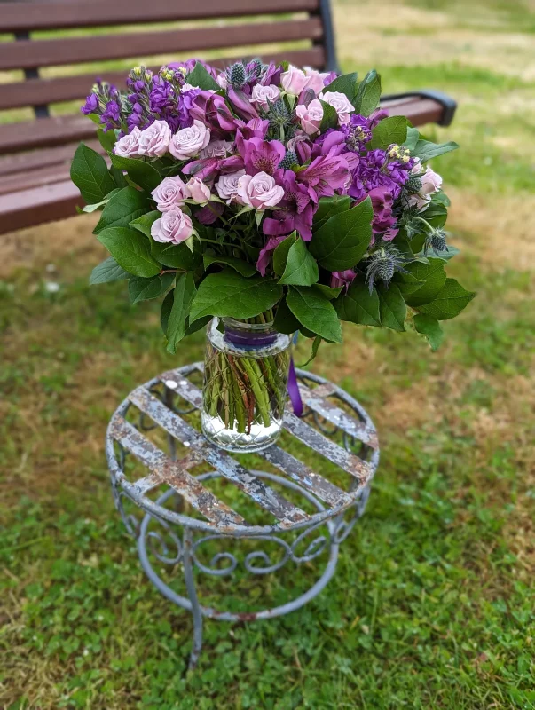 A rustic-chic wedding floral design, featuring roses, vibrant purple alstroemerias, and delicate blue thistles, creating a wonderful springtime ambiance.