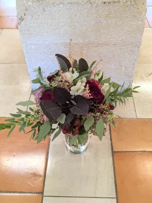 Sophisticated rustic floral arrangement with burgundy roses, white alstroemeria, and eucalyptus.