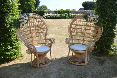 Deux chaises paon en rotin décorées de roses poudrées et eucalyptus, créant une scénographie de cérémonie bohème en jardin.