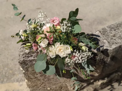 Composition florale champêtre aux roses crème, œillets roses et eucalyptus, posée sur une pierre naturelle en extérieur.