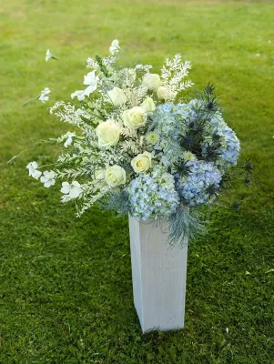 Composition florale champêtre élégante avec roses blanches, hortensias bleus et chardons pour un mariage printanier.