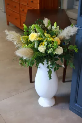 Grande composition florale bohème dans un vase blanc, avec roses jaunes, pampas et plume de paon.