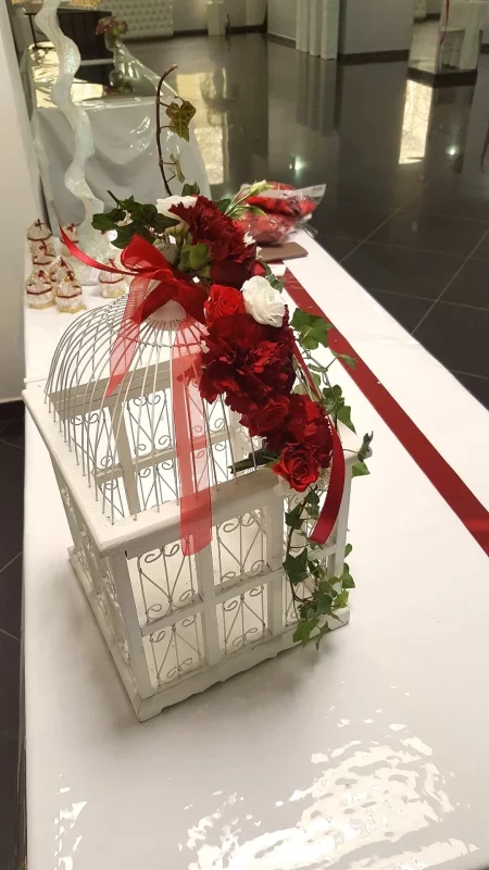 Composition florale classique avec roses rouges et blanches, œillets et lierre sur une cage décorative blanche, mariage.