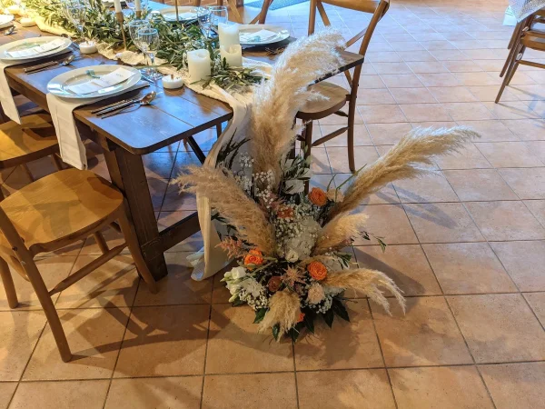 Grande composition florale bohème au sol avec herbe de la pampa, roses orange et feuillage, pour un mariage.