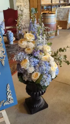 Composition florale de mariage classique dans une grande urne noire avec des roses crème, des hortensias bleus et du feuillage.
