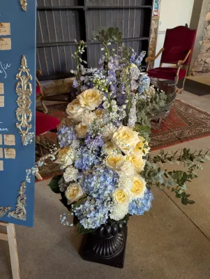 Composition florale de mariage classique dans une grande urne noire avec des roses crème, des hortensias bleus et du feuillage.