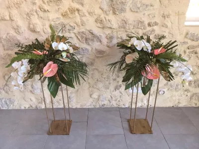 Deux compositions florales exotiques sur colonnes dorées avec orchidées blanches, anthuriums roses et feuillage tropical