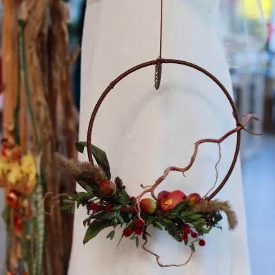 Couronne florale suspendue bohème avec petites pommes rouges, baies, feuillage et éléments séchés.