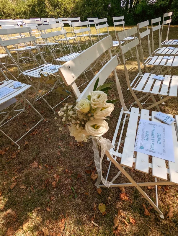 Petits bouquets de renoncules crème et gypsophile blanche attachés aux chaises pour la cérémonie en plein air, style champêtre.