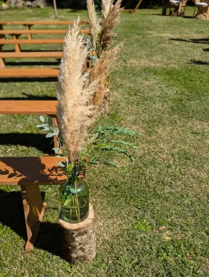 Detail d'une decoration d'allee de ceremonie avec pampas et eucalyptus dans un vase en verre sur une buche en bois.