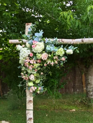 Décoration florale champêtre pour une arche de mariage, avec roses, hortensias et eucalyptus sur une structure en bois.