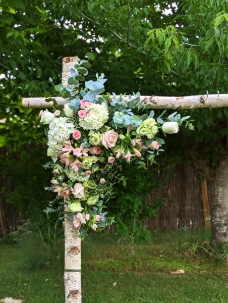 Décoration florale champêtre pour une arche de mariage, avec roses, hortensias et eucalyptus sur une structure en bois.