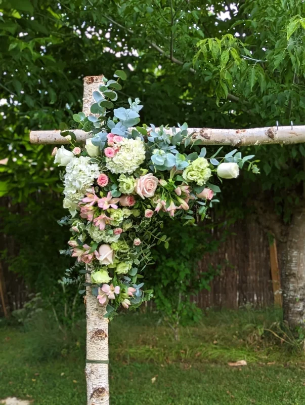 Décoration florale champêtre pour une arche de mariage, avec roses, hortensias et eucalyptus sur une structure en bois.