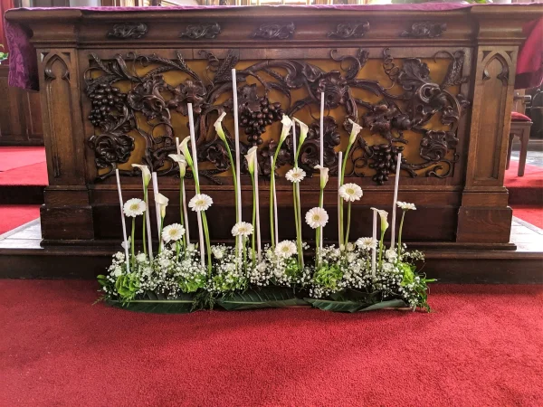 Décoration d'autel de mariage classique, avec des rangées d'arums, gerberas et gypsophile entourant des bougies hautes.